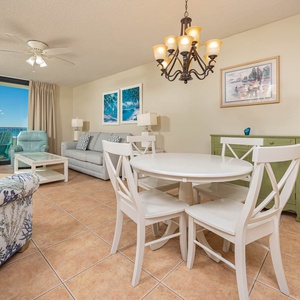 Living area features a light gray sofa with queen sleeper, dining table, and access to the balcony with views of the beach