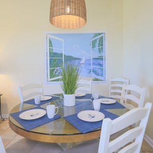 Dining table set for family meals features nautical dishware, surrounded by light-colored chairs and a beach mural