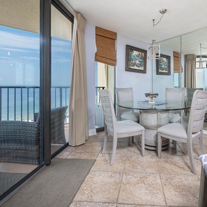 Bright dining area features a glass table surrounded by six chairs, with a view of the beach