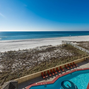 A serene view showcases the sparkling pool surrounded by lounge chairs, leading to a pristine beach and calm blue waters