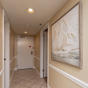 This welcoming hallway features light beige walls, elegant ship artwork, and a tiled floor, leading to inviting rooms