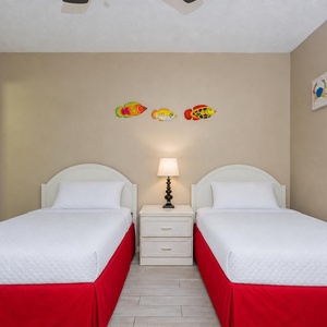 This guest bedroom features two twin beds with bright red bed skirts and colorful fish decor, creating a cheerful atmosphere