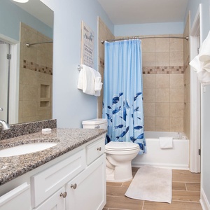 Guest bathroom featuring a granite countertop, a tub/shower combo with a blue fish-patterned curtain, and fresh towels