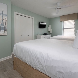 Soothing guest bedroom featuring two queen beds, a TV, and beach decor
