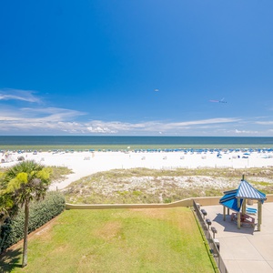 Lush green lawn leads to a vibrant pool area with blue lounge chairs and shaded cabanas, just steps from the beach