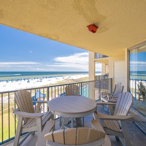The balcony offers a serene view of the beach with white sand and blue umbrellas, perfect for relaxation and enjoyment