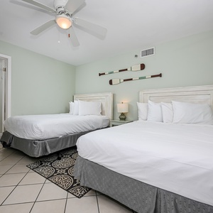 This guest bedroom features two queen beds, a ceiling fan, and nautical decor, creating a relaxed coastal atmosphere