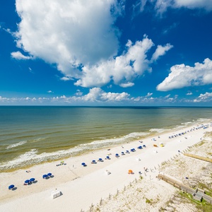 Enjoy the refreshing coastal breeze from your balcony, with views of the inviting shoreline and vibrant beach umbrellas