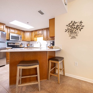Warm wooden cabinetry complements the kitchen's sleek countertops, featuring a breakfast bar with two stools