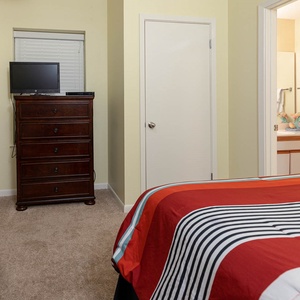 Guest bedroom features two comfortable queen beds, a wooden dresser, and a view into a bathroom area