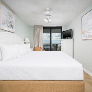 The master suite featuring a king bed, a TV, and access to a balcony with views of the gulf