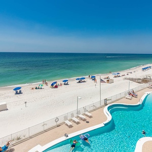 This vibrant beachfront view showcases a sparkling pool area with lounge chairs and umbrellas, perfect for relaxation