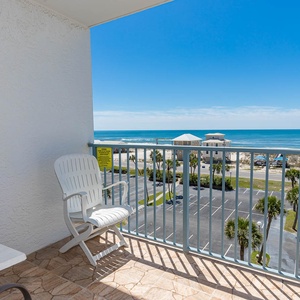 Enjoy a relaxing view from this balcony with a white chair, overlooking the beach and vibrant blue waters