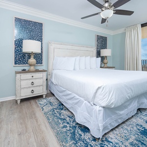 The master suite features a king bed, coastal artwork, and access to a balcony with a view of the beach