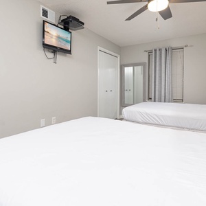 Guest room featuring two queen beds, a wall-mounted TV, and a large mirror, complemented by soft gray tones and natural light