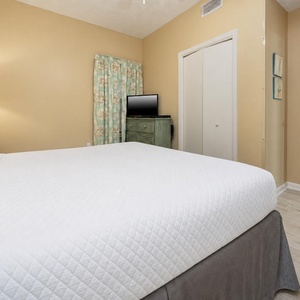 Brightly lit bedroom featuring a plush king bed, a decorative lamp, and a TV on a charming green dresser