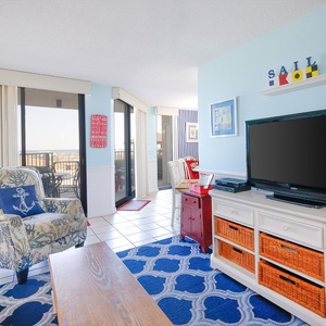 Living area featuring a cozy floral armchair, a TV, twin bunk, and access to a balcony with a view of the beach front