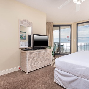 Unwind in this comfortable master bedroom featuring a TV, stylish dresser, king bed, and beachfront balcony access