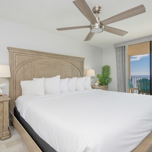 Cozy master bedroom featuring a king bed, stylish wooden furniture, and a balcony with seating overlooking the beach