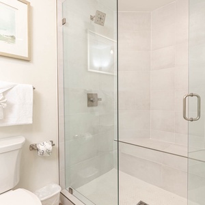 This bathroom features a sleek glass walk-in shower, fresh white towels, and soft neutral tones for a refreshing retreat