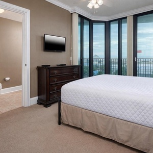 Bright guest bedroom featuring a queen bed, elegant dresser, and large balcony windows offering a scenic view