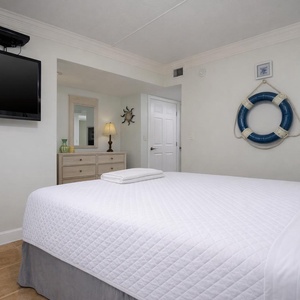 This inviting room features a comfortable bed, a mounted TV, and coastal decor, perfect for a relaxing getaway