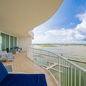 Relax on the spacious balcony with blue seating, enjoying serene water views and gentle coastal breezes