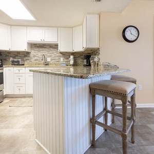 Kitchen features sleek cabinetry, a granite countertop breakfast bar with seating, and a view into the master suite