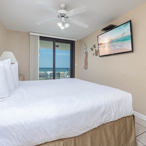 The master bedroom featuring a plush king bed, ceiling fan, and a TV, with sliding doors leading to a balcony view