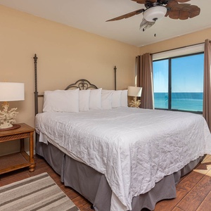 The master bedroom features a plush king bed with a stunning beachfront view through large windows, perfect for relaxation