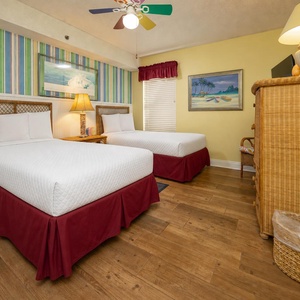 This cheerful guest bedroom features two twin beds with vibrant red skirts, colorful striped wallpaper, and beach decor