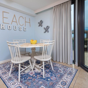 Bright blue walls complement a round dining table with white chairs, accented by a view of the beach through large windows