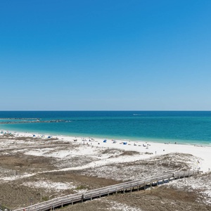 Vibrant turquoise waters stretch along the beach, framed by white sand and a wooden boardwalk leading to the shore