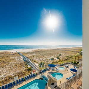 The pool area, sandy beach, and the expansive gulf, viewed from the balcony under a bright sunny sky