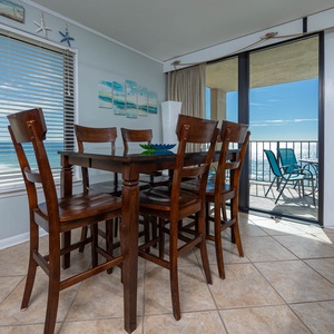 This dining area features a stylish wooden table with high-backed chairs and a beautiful view of the sparkling water beyond