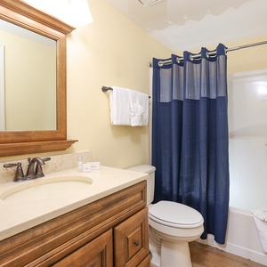 The guest bathroom features warm wood cabinetry, a large mirror, and a relaxing shower area with a navy blue curtain