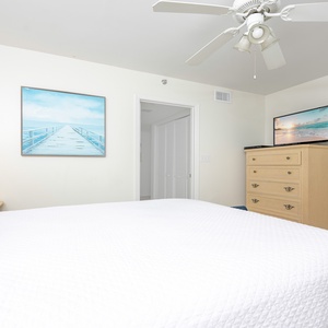 Bright guest bedroom featuring a queen bed, light-colored furniture, a TV, and coastal artwork that enhances the serene vibe