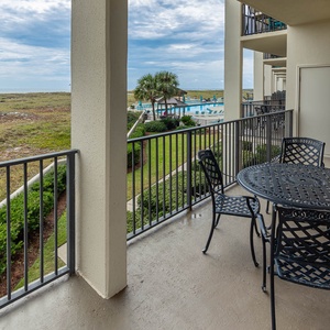 Balcony with a round table and chairs overlooks lush greenery and a pool area, creating a serene outdoor retreat