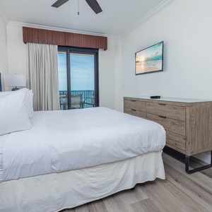 Retreat to the cozy master bedroom featuring a king bed, stylish decor, and a view of the beach from the balcony