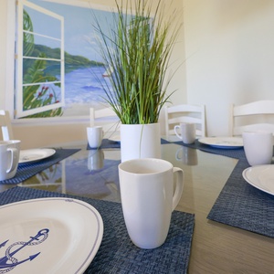 A dining table set with nautical-themed plates and mugs, accented by a vibrant mural of a serene beach view