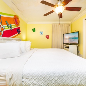 Brightly colored decor complements the spacious bedroom featuring a large king bed, a ceiling fan, and a flat-screen TV