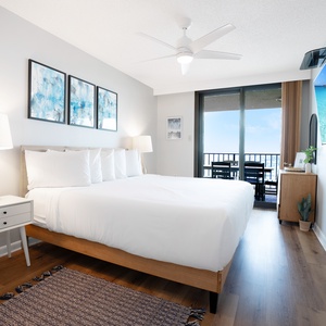 Bright master bedroom featuring a king bed, modern decor, and the balcony view with outdoor seating overlooking the beach