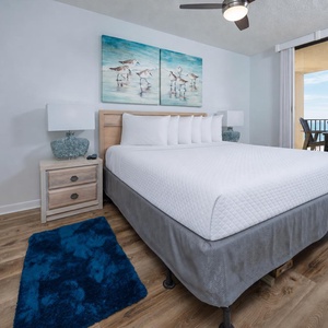 Brightly decorated master bedroom featuring a king bed, stylish lamps, and a balcony with a view of the beach