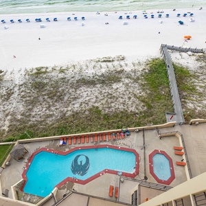 Balcony view showcases the vibrant pool area with lounge chairs and a pathway leading to the beach, framed by white sand