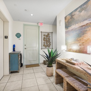 The welcoming entryway features a beautiful coastal painting, stylish lighting, and a decorative plant, creating a warm tone