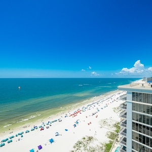 Enjoy breathtaking views from your balcony, where vibrant beach umbrellas line the shore under a clear blue sky