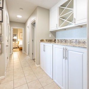 Discover a welcoming hallway adorned with framed photos, leading to cozy bedrooms and stylish wet bar