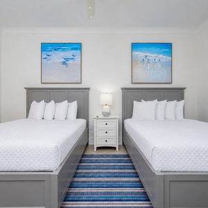 Tranquil guest bedroom featuring two queen beds, coastal artwork, and a soft area rug for added warmth