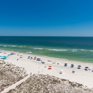 This inviting view showcases a pristine beach with colorful umbrellas and a sparkling pool, perfect for a relaxing getaway