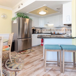 Bright kitchen featuring stainless appliances, granite countertops, and the dining area with colorful patterned chairs